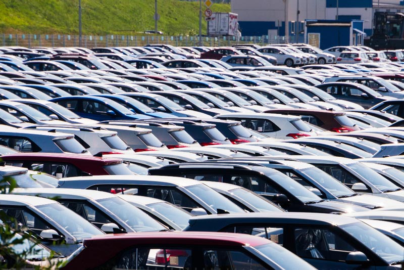 Ein dicht bepackter Parkplatz bei Gebrauchtwagen Ankauf Soest ist mit Reihen geparkter Autos in verschiedenen Farben, hauptsächlich Weiß und Rot, unter einem sonnigen blauen Himmel gefüllt.
