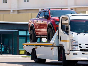 Ein rotes Pickup wird in einer sonnigen städtischen Umgebung auf einen weißen Abschleppwagen von Unfallwagenankauf Soest verladen.